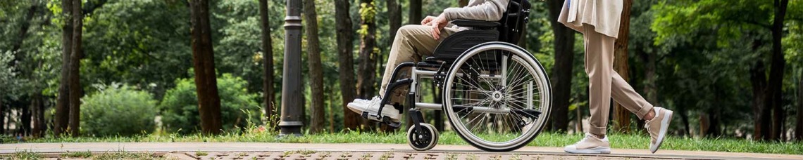 senior woman with husband in wheelchair walking in park