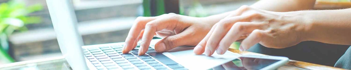 Person typing on laptop with window in background